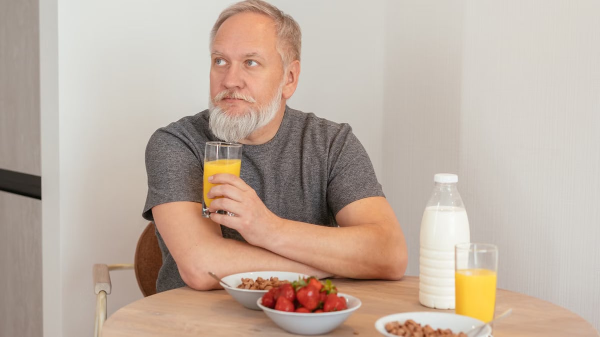 Elderly man with a beard enjoying a nutritious breakfast with orange juice, cereal, and strawberries.